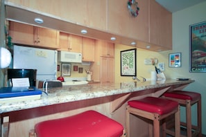 A kitchen with wooden cabinets, a granite countertop, and red bar stools.