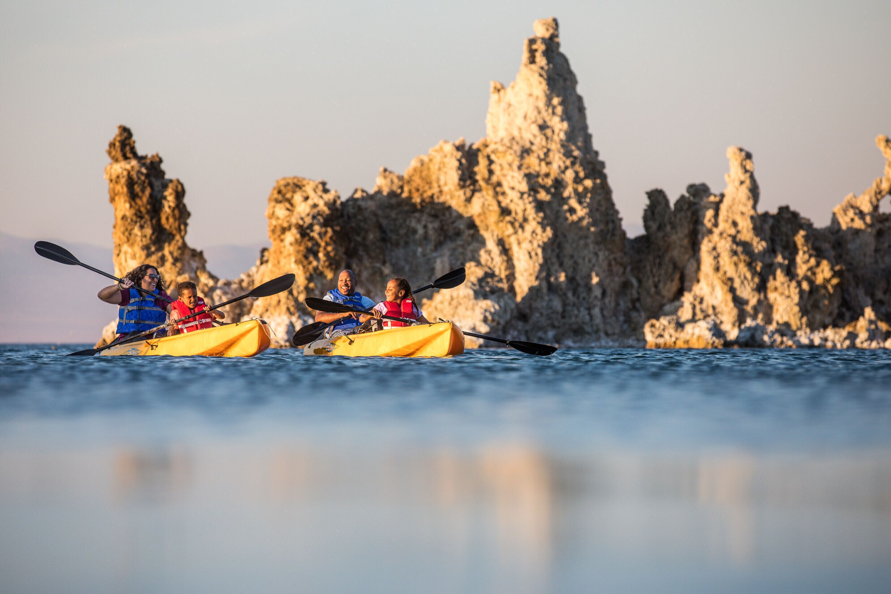 Deux personnes pratiquent le kayak dans un kayak jaune, avec un paysage rocheux en arrière-plan.