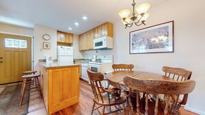 A kitchen with wooden cabinets, a dining table with chairs, a refrigerator, a microwave, and a chandelier. - Homey & Updated Condo near The Village, Private Balcony. Hot Tub On-site (Mammoth Lakes)