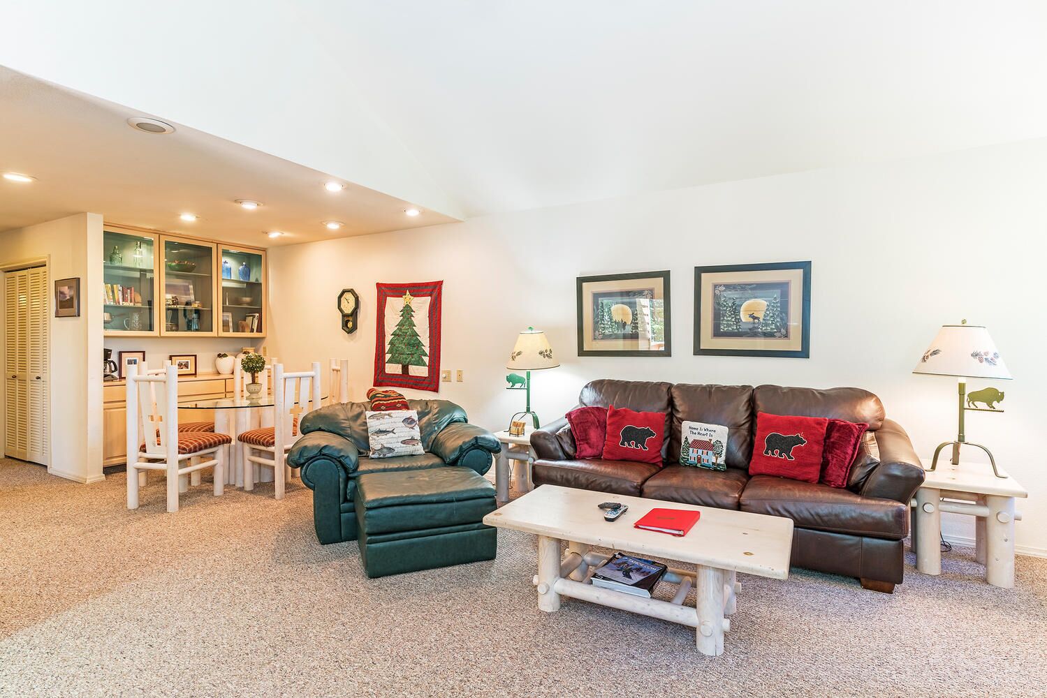 A cozy living room with a brown leather sofa, a green armchair, and a white coffee table. There are framed pictures on the wall and a Christmas tree decoration.