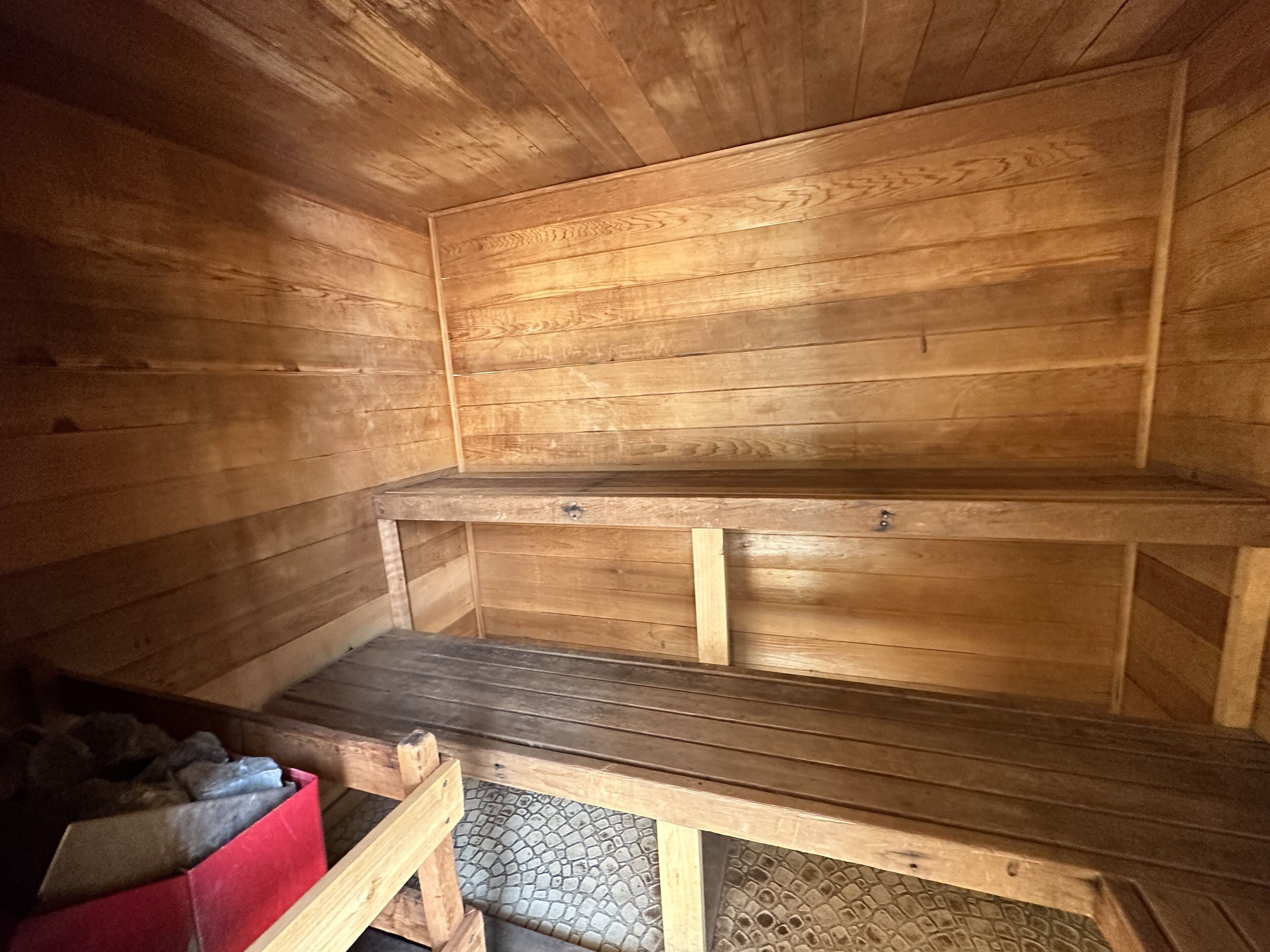 Uma sauna de madeira com bancos e uma caixa de armazenamento vermelha.