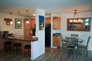 Una cucina con mobili in legno, un frigorifero, un tavolo da pranzo con sedie e lampade a sospensione.