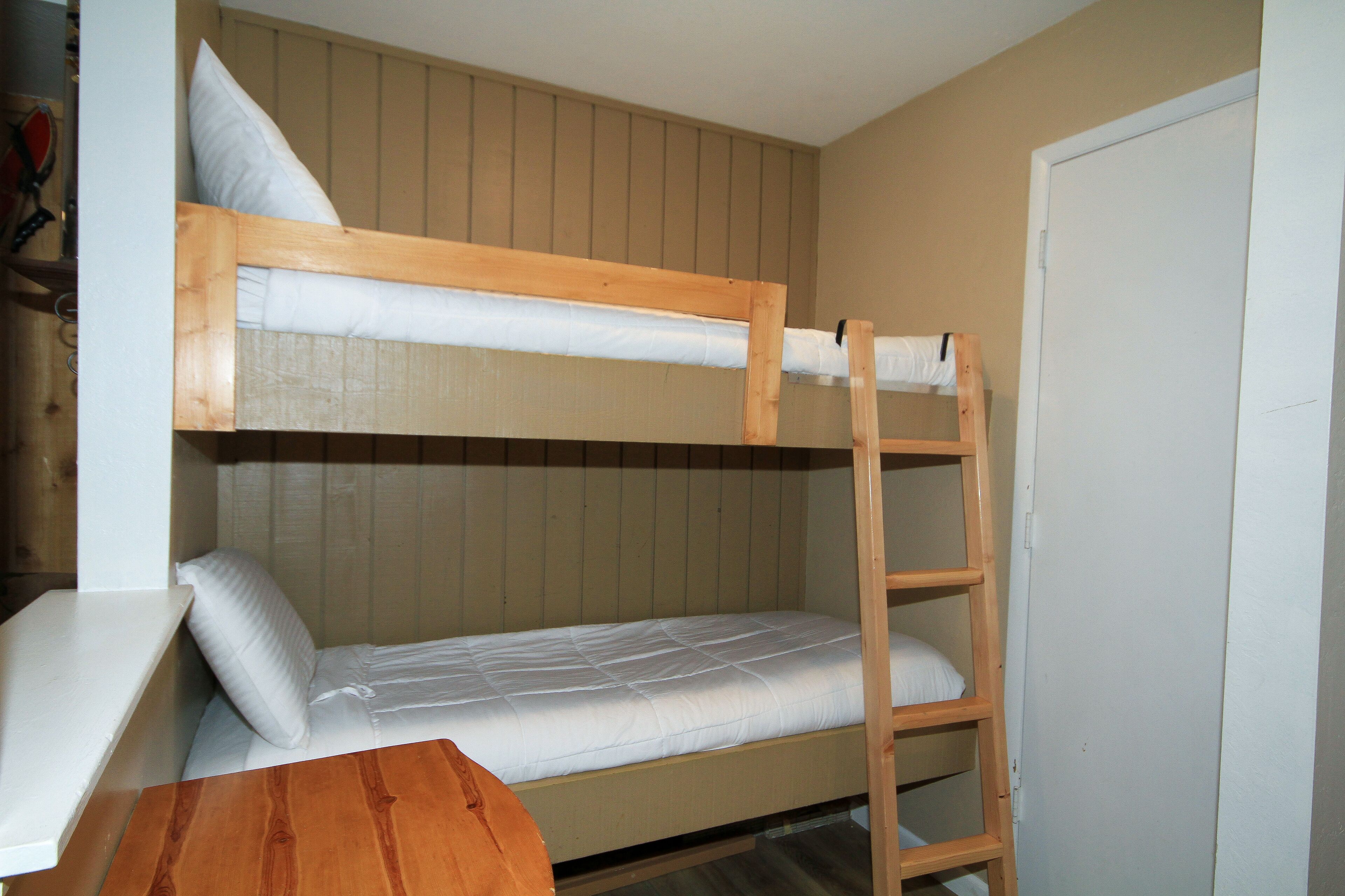 A bunk bed room with a wooden ladder, a small table, and a white door.