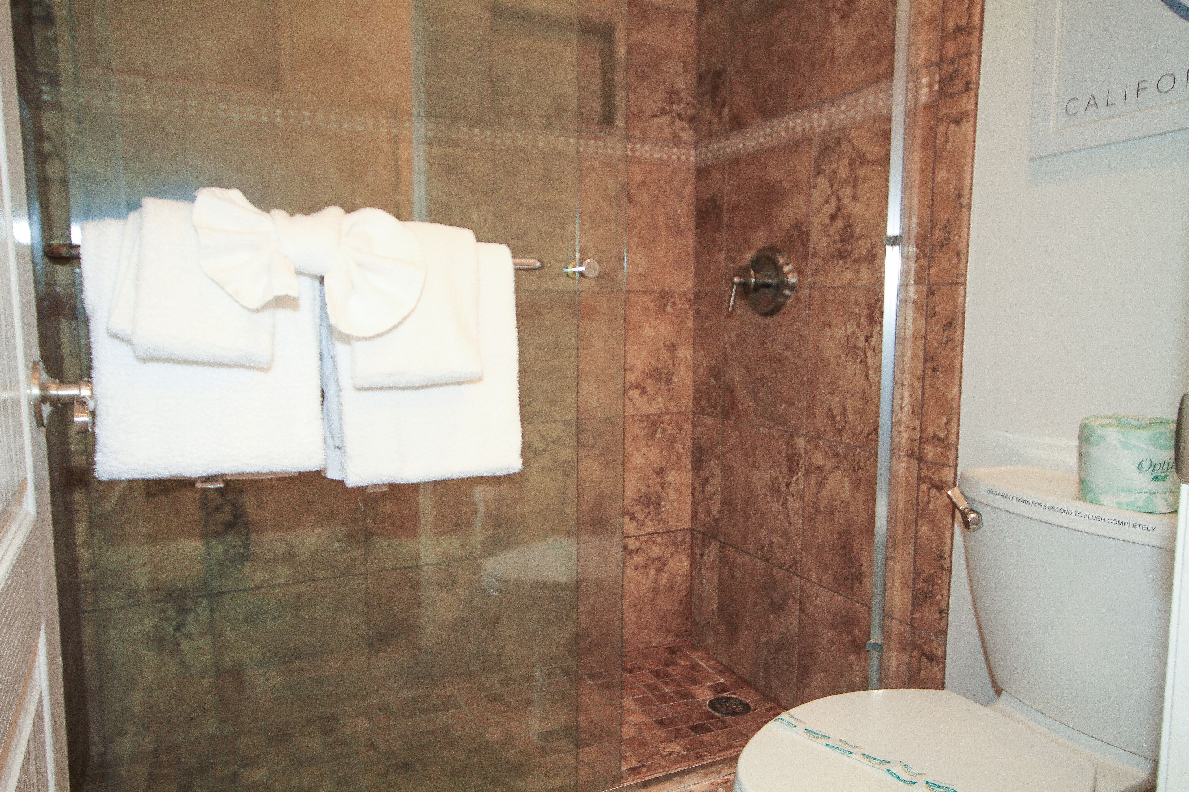 A bathroom with a glass-enclosed shower, a toilet, and a towel rack with folded towels.