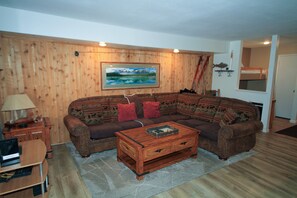 Un soggiorno con parete in legno, un quadro di grandi dimensioni, un divano marrone con cuscini rossi, un tavolino da caffè in legno e una scrivania con una lampada.