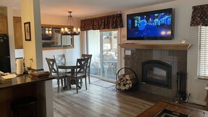 A modern kitchen with a dining area, a fireplace, and a TV mounted on the wall.