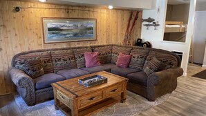 A cozy living room with a wooden wall, a large framed picture, a brown sofa with patterned cushions, a wooden coffee table, and skis leaning against the wall.