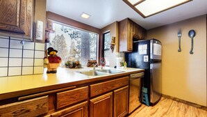 Une cuisine avec des meubles en bois, un réfrigérateur en acier inoxydable, un évier et une fenêtre avec des stores.