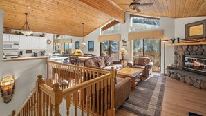 A spacious living area with a wooden ceiling, a stone fireplace, and large windows offering a view of the outdoors. - 93 Bitterbrush | 4BR/3.5BA Incline Village | Lake Views (Incline Village)