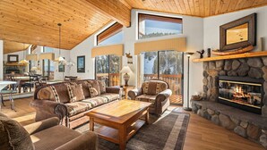 A spacious living room with a stone fireplace, leather furniture, and large windows offering a view of the outdoors. - 93 Bitterbrush | 4BR/3.5BA Incline Village | Lake Views (Incline Village)