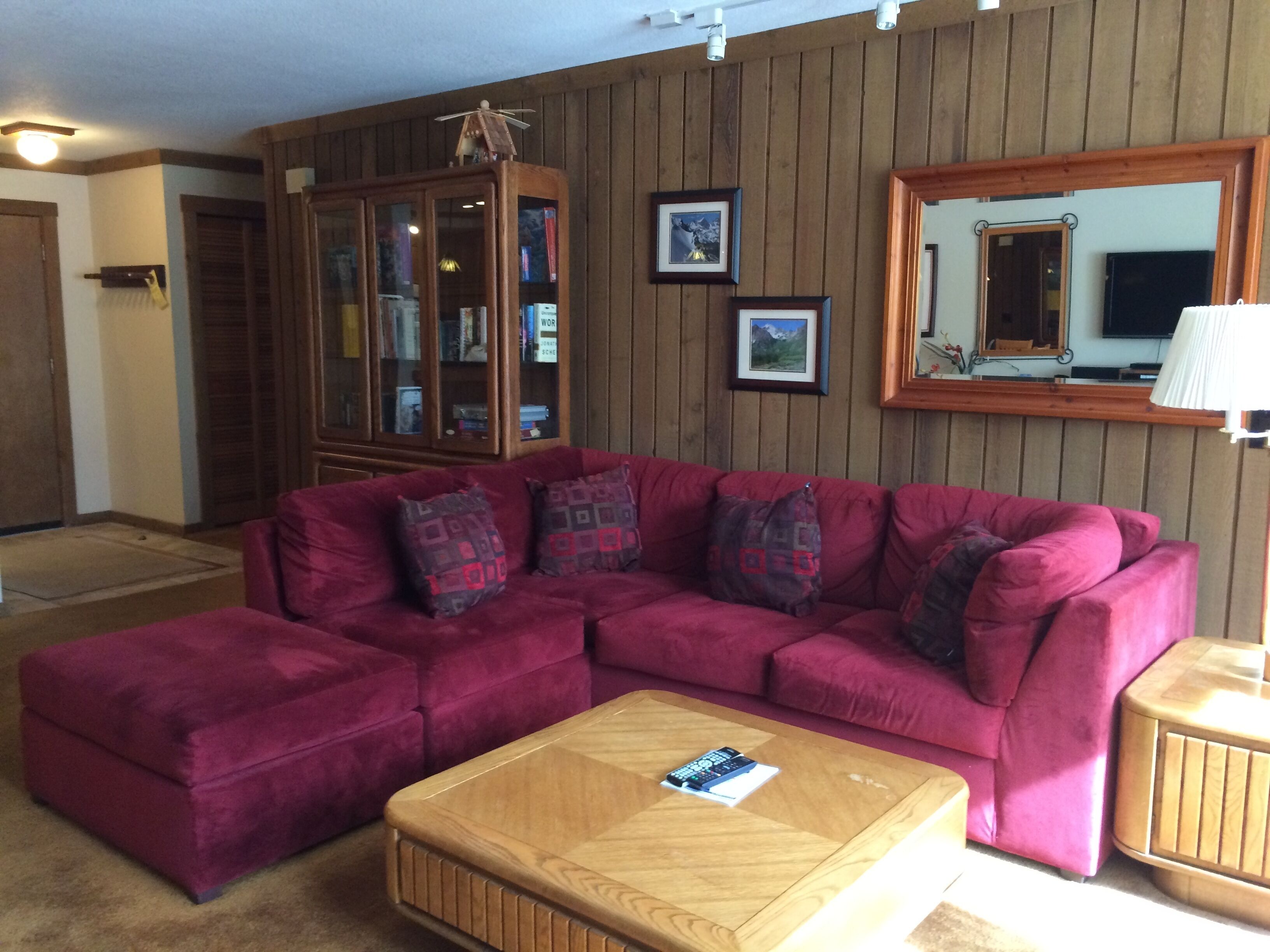 A living room with a sectional sofa, a coffee table, a wooden cabinet, and a mirror on the wall.