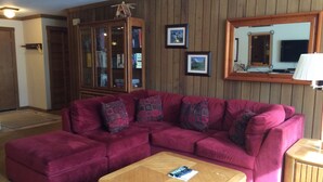 Una sala de estar con un sofá modular, una mesa de centro, un aparador de madera y un espejo en la pared.