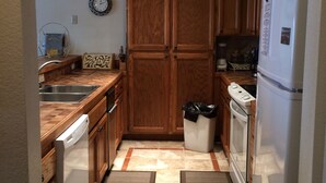 Una cocina compacta con armarios de madera, un lavamanos de acero inoxidable, lavavajillas, refrigerador y microondas.