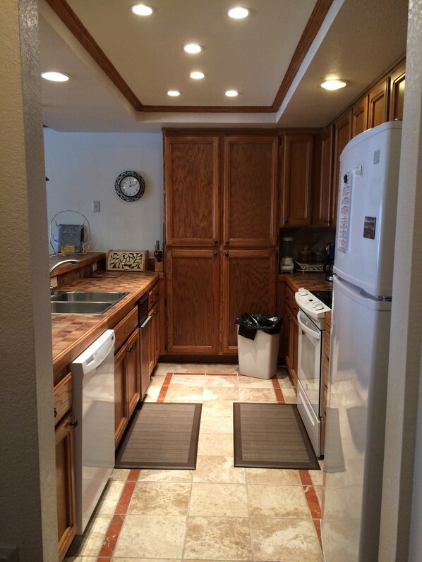 A compact kitchen with wooden cabinets, a stainless steel sink, a dishwasher, a refrigerator, and a microwave. - Mountainback #71 2 Bedroom 2 Bath (Mammoth Lakes)