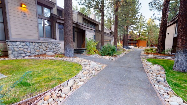 A residential area with a paved driveway, stone-lined borders, and a row of houses with a stone facade and large windows.