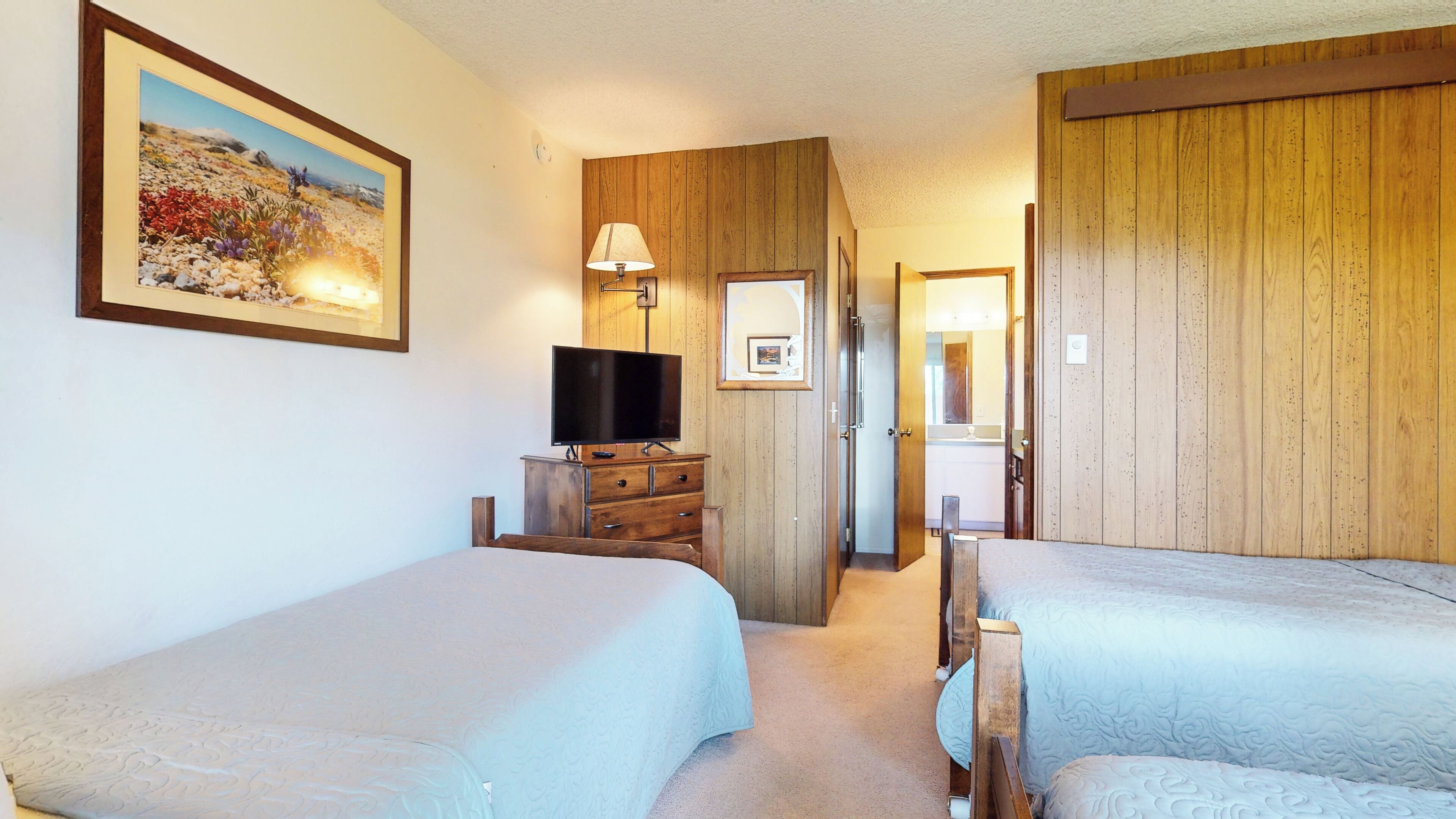 A hotel room with two beds, a TV, a dresser, and a painting on the wall.
