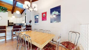 A dining area with a wooden table and metal chairs, a kitchen in the background, and artwork on the walls. - Spacious Home, Wood-Burning Fireplace, On Shuttle Route & Walk to Downtown (Mammoth Lakes)