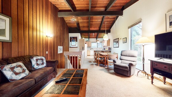 A cozy living room with a wooden ceiling, a sofa, a coffee table, and a TV.