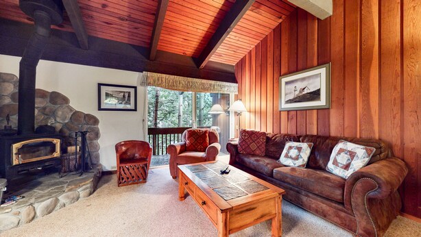 A cozy living room with a stone fireplace, leather armchairs, a wooden coffee table, and a large window offering a view of trees. - Spacious Condo, Near Biking Trails. Great Summer Amenities & Pool On-site (Mammoth Lakes)