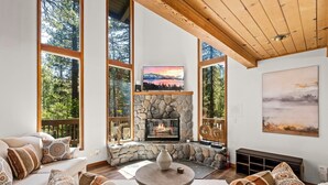 A cozy living room with a stone fireplace, large windows, and a comfortable seating area.
