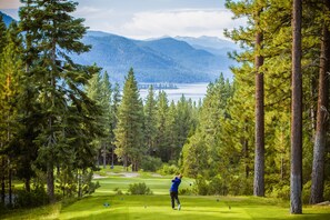 En golfbana med utsikt över en sjö och berg i bakgrunden.