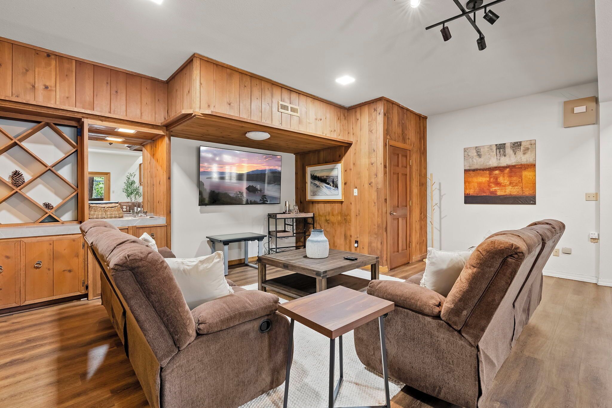 A cozy living room with wooden paneling, a large window, a fireplace, and a dining area with a table and chairs.