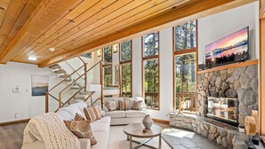 A spacious living room with a large sectional sofa, a stone fireplace, and a staircase leading to an upper level.