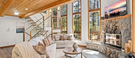 Un salón espacioso con un sofá seccional grande, una chimenea de piedra y una escalera que conduce a un nivel superior.