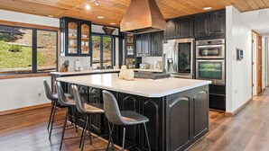 A modern kitchen with a large island, dark cabinetry, and stainless steel appliances.
