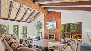 A modern living room with a large sectional sofa, a fireplace, and large windows offering a view of the outdoors.