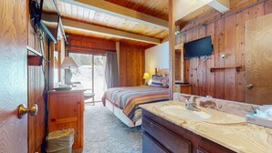 Un dormitorio de cabaña de madera con una cama, mesita de noche, lámpara y un espejo grande.