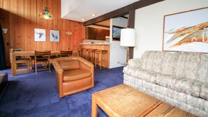 A living room with a brown leather armchair, a patterned sofa, a wooden coffee table, and a dining area with wooden furniture. - Mammoth Ski & Racquet Club #129, 1 Bdrm + Loft (Mammoth Lakes)