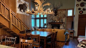 A dining area with a wooden table and chairs, a stone fireplace, and a mounted bison head. - Mountainback #79, Loft, Den (Mammoth Lakes)