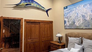A bedroom with a bed, a nightstand, a lamp, a wooden wardrobe, a map on the wall, and a large fish decoration. - Mountainback #79, Loft, Den (Mammoth Lakes)