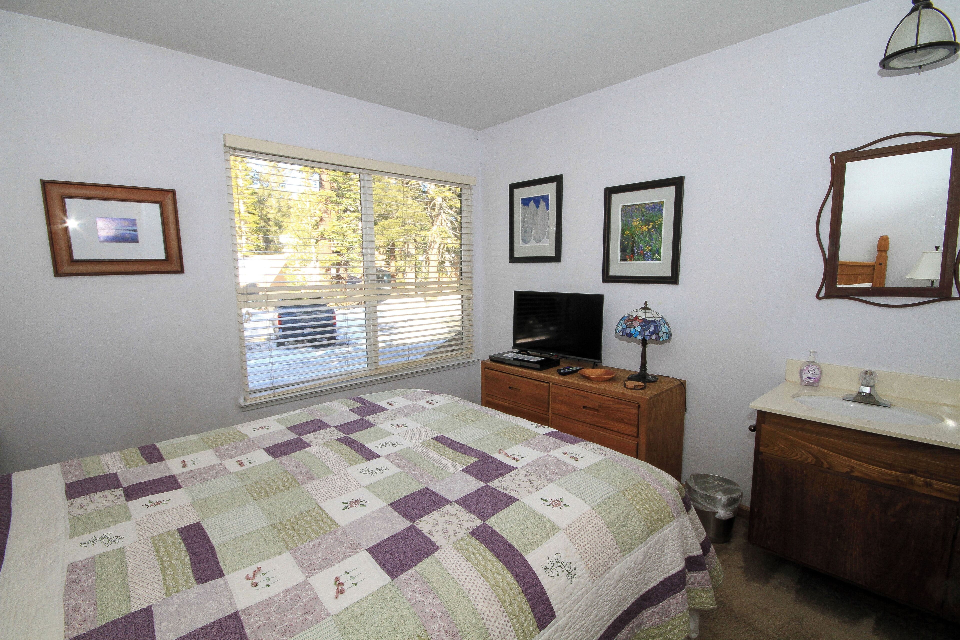 A bedroom with a bed, dresser, vanity, and window with blinds.