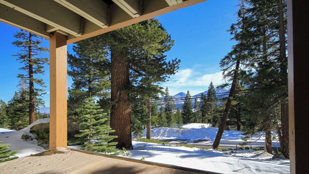 Una terraza de madera con vistas a terreno nevado y altos pinos.
