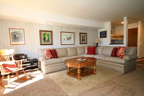 A living room with a beige sofa, a wooden rocking chair, a coffee table, and framed artwork on the walls.