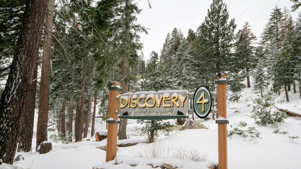A wooden sign with the text "Discovery Condominiums" and a directional arrow. - Discovery 4 #113 1 Bedroom 1 Bath (Mammoth Lakes)