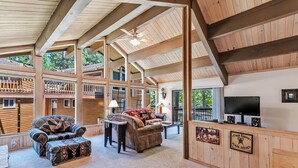 A spacious living area with a high ceiling, wooden beams, a fireplace, a television, and a sign indicating a tour shop. - 10NSE | 3BR/2.5BA Incline Village, Mtn Views & BBQ (Incline Village)