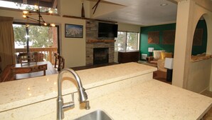 Una cocina con chimenea de piedra, un comedor con mobiliario de madera y una sala de estar con pared verde y paneles decorativos.