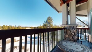 Un balcon doté d’un mur en pierre, d’une balustrade en bois et offrant une vue sur un paysage enneigé, avec des arbres et des montagnes en arrière-plan.