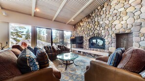 A cozy living room with stone walls, a fireplace, comfortable seating, and large windows.