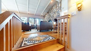 Eine Treppe führt zu einem Wohnbereich mit Steinwand, einer Couch und einer Holzgeländer.