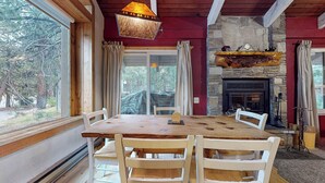 Uma sala de jantar com mesa e cadeiras de madeira, lareira de pedra e vista para o exterior.