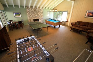 Relax and unwind in this spacious room, featuring a foosball table, pool table, and billiards table, along with comfortable seating and a dining area.