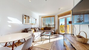 Relax in the spacious living area with a sofa, coffee table, and dining table, surrounded by large windows and a large mirror.