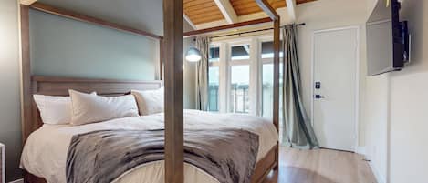 Une chambre avec un plafond en bois, un grand lit avec une literie blanche, un téléviseur fixé au mur et une porte avec une serrure.