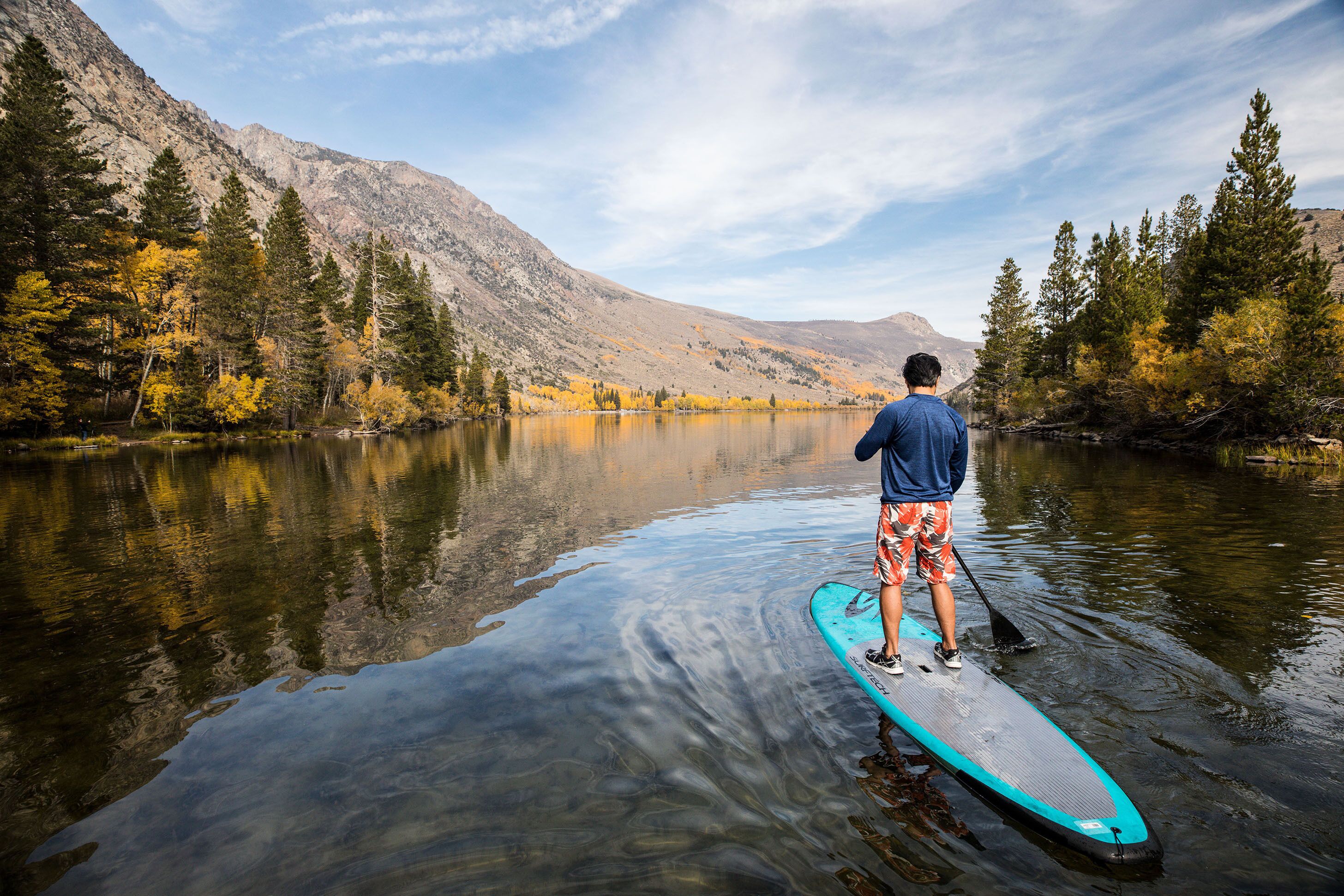 Une personne se tient debout sur une planche à pagaie dans un lac paisible, entouré de montagnes.