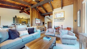 Ein geräumiges Wohnzimmer mit hoher Decke, sichtbaren Holzbalken, einem Kamin und einer gemütlichen Sitzecke mit Sofas und einem Couchtisch.