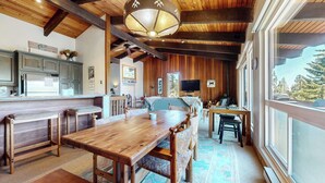 Ein rustikales Lodge-Interieur mit Holztisch, Bänken, einer Küchenzeile und einem großen Fenster mit Blick ins Freie.
